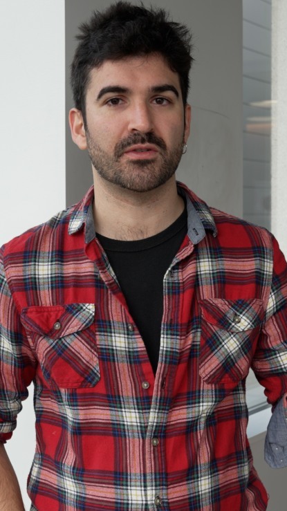 head and shoulders picture of dark haired person with beard wearing red plaid shirt facing the camera